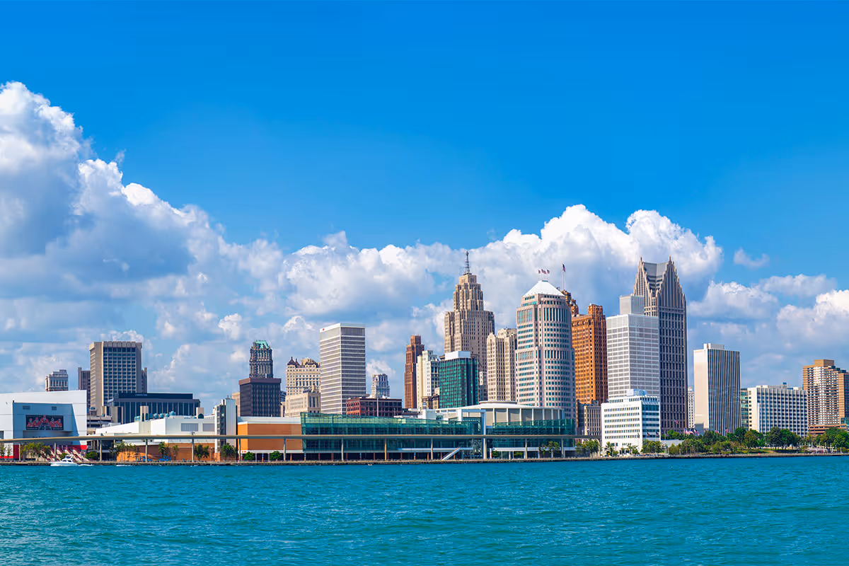 Panoramic view of Detroit skyline with blue sky and clouds over calm water.