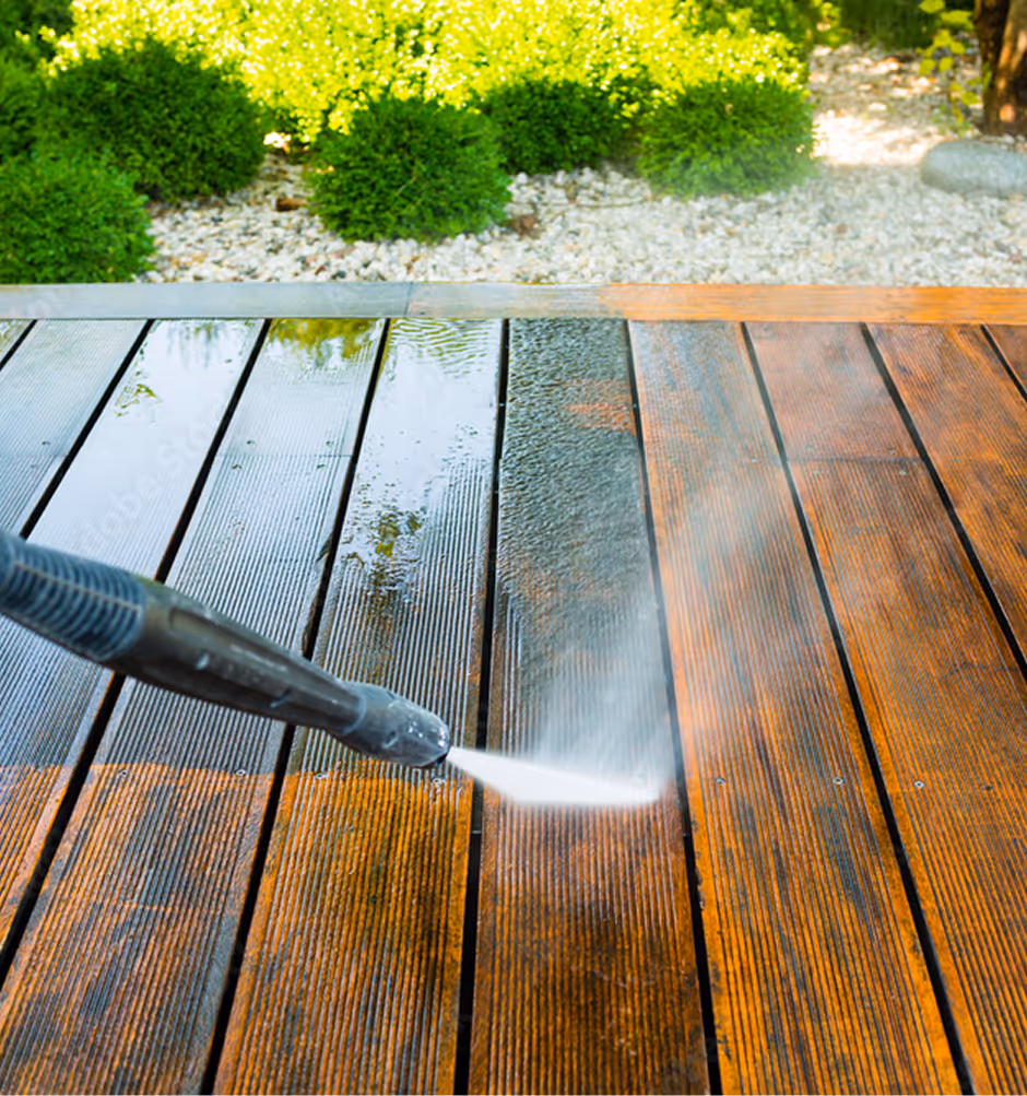 Close-up of a power washing nozzle spraying water to clean a wooden deck, showing a clear contrast between cleaned and dirty wood.
