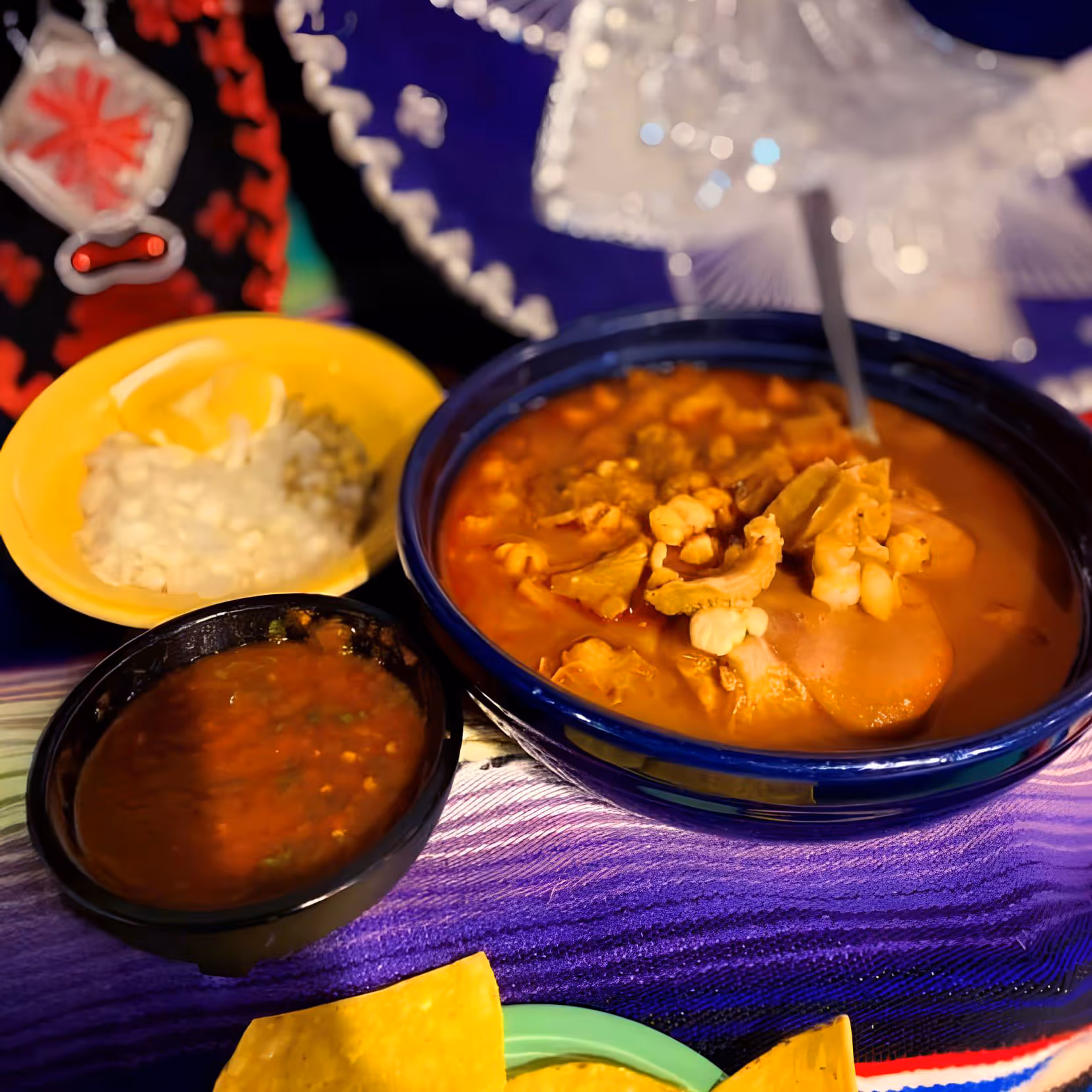 A colorful Mexican dish of menudo with tripe and hominy in a blue bowl. 