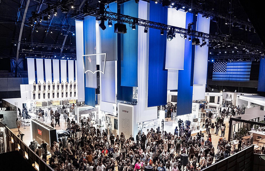 A sleek red Ferrari sports car displayed on an illuminated white platform at night, with red ambient lighting on nearby buildings and a glowing inspirational quote projected on a wall in the background.