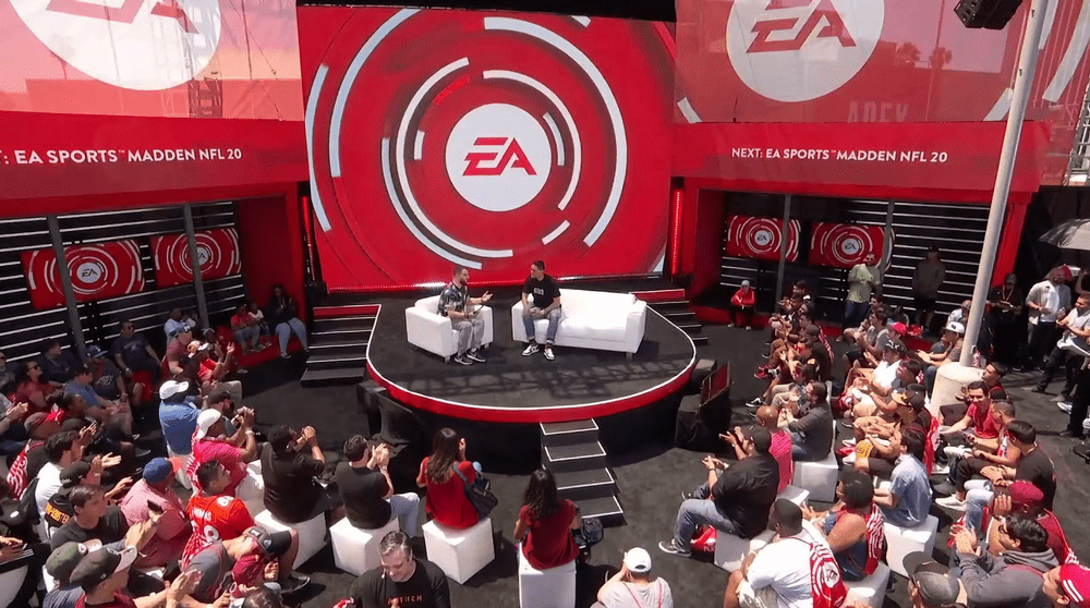 Large-scale event stage design featuring prominent EA logos and red circular motion graphics on a massive digital backdrop, with an audience seated in the foreground.