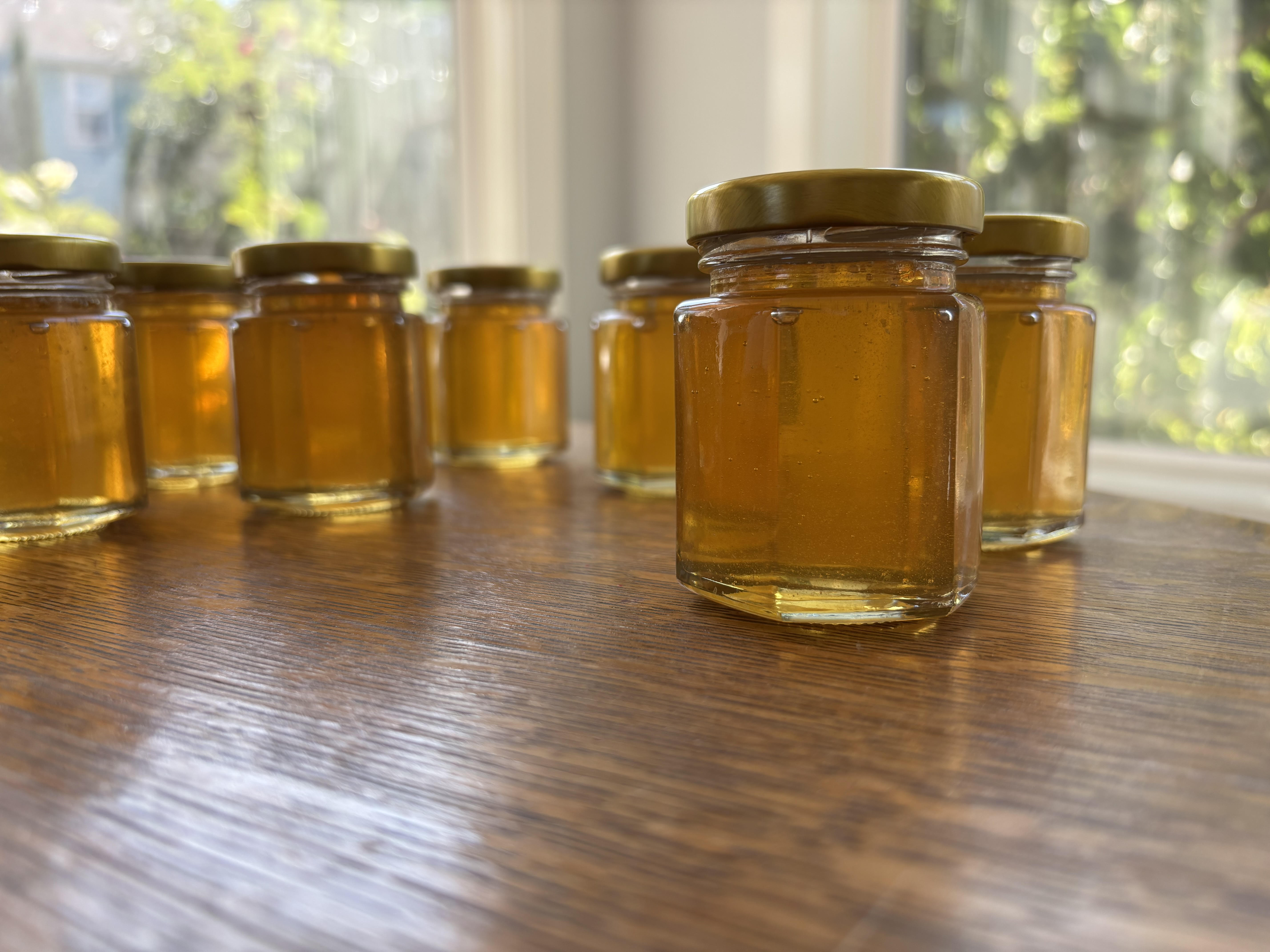 Small glass jars filled with golden honey arranged on a wooden table near a window.
