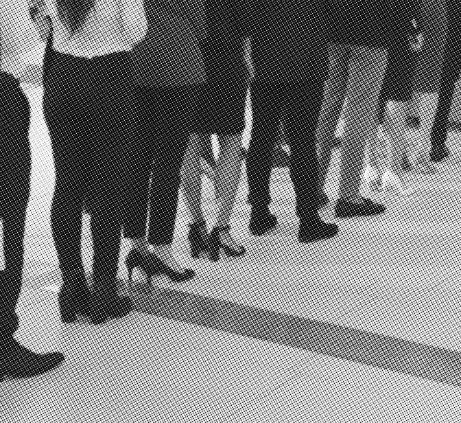 grayscale halftone image of a line up of people waiting at a desk, only showing waist down