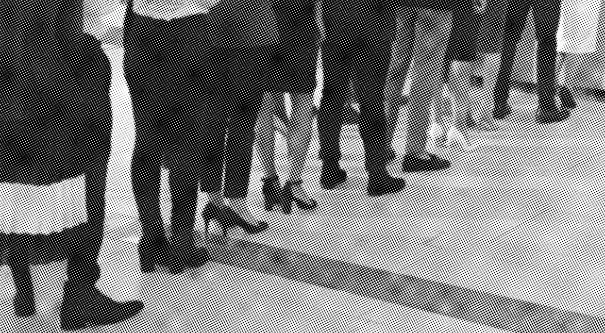 grayscale halftone image of a line up of people waiting at a desk, only showing waist down