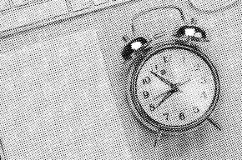 grayscale halftone image of a round alarm clock a piece of graph paper and a keyboard on a plain backdrop