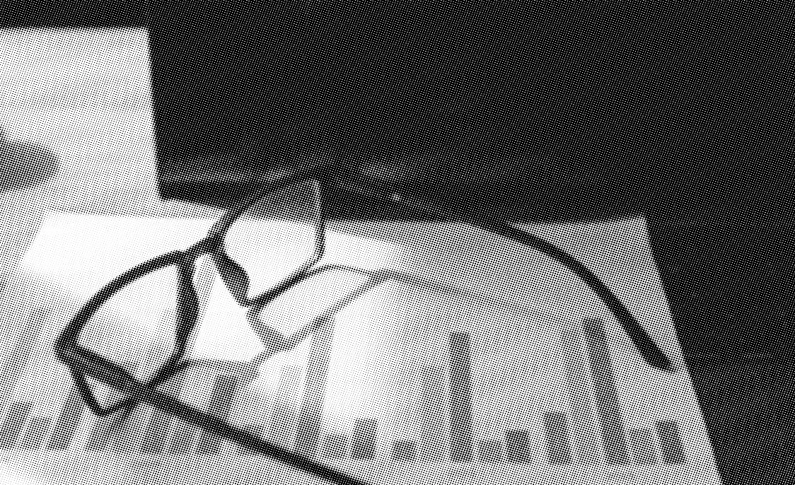 grayscale halftone image of glasses on top of papers with bar graphs on top of a laptop