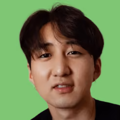 Close-up of a man with dark hair and a neutral expression against a green background.