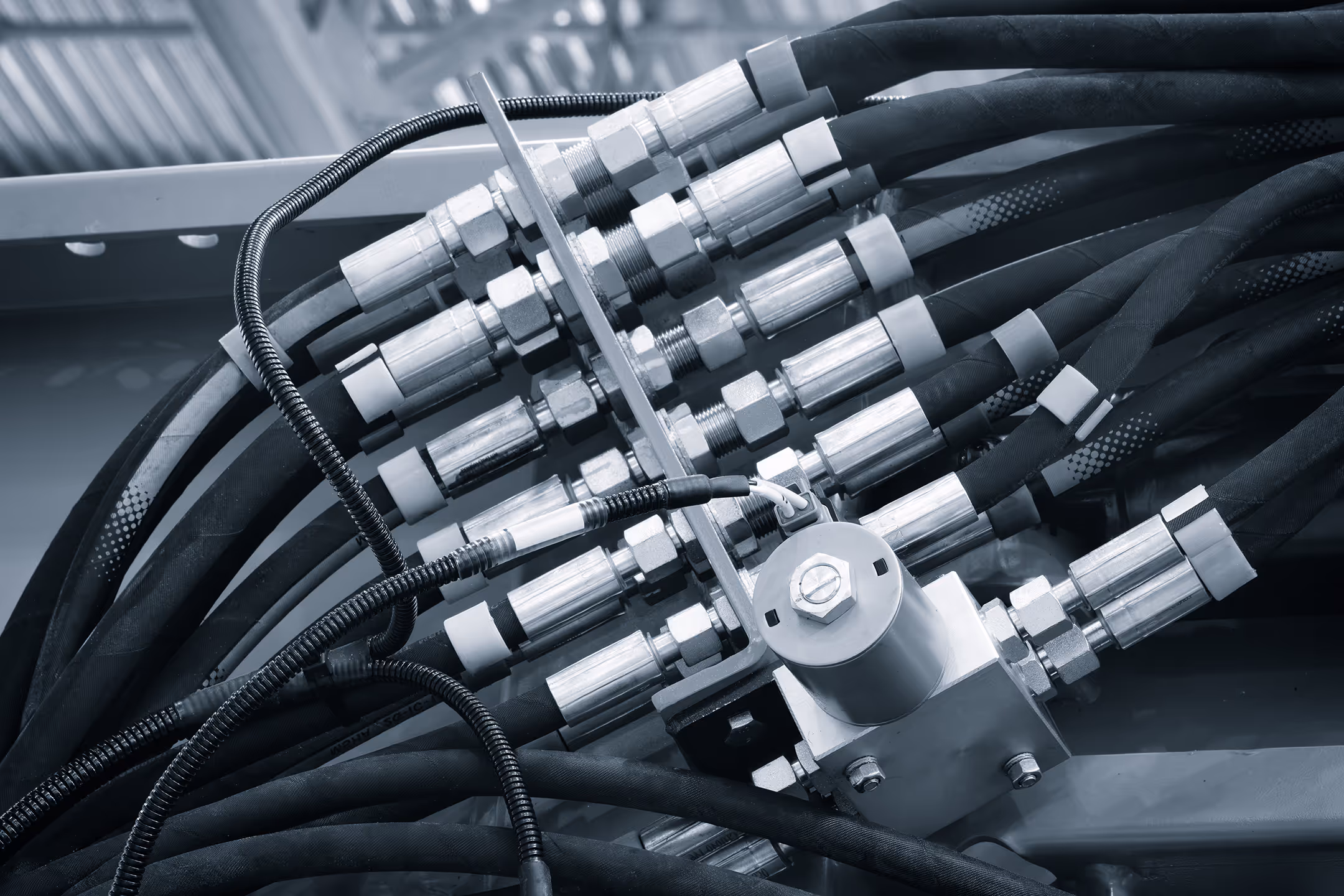 Close-up of hydraulic hoses connected to metal fittings and a valve block in an industrial machine.