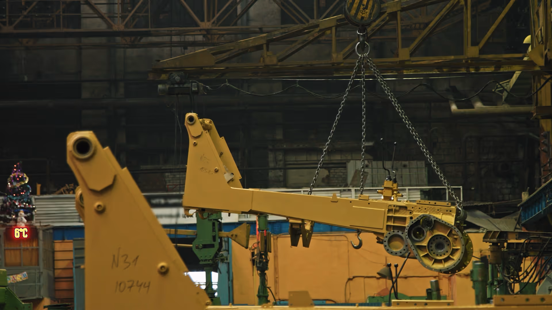 Yellow industrial equipment part suspended by chains inside a large factory.