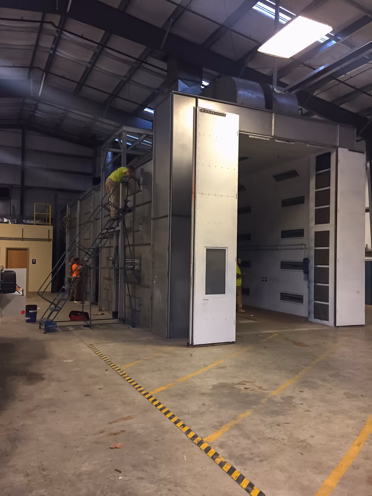 Workers assembling or inspecting a large industrial metal structure inside a warehouse.