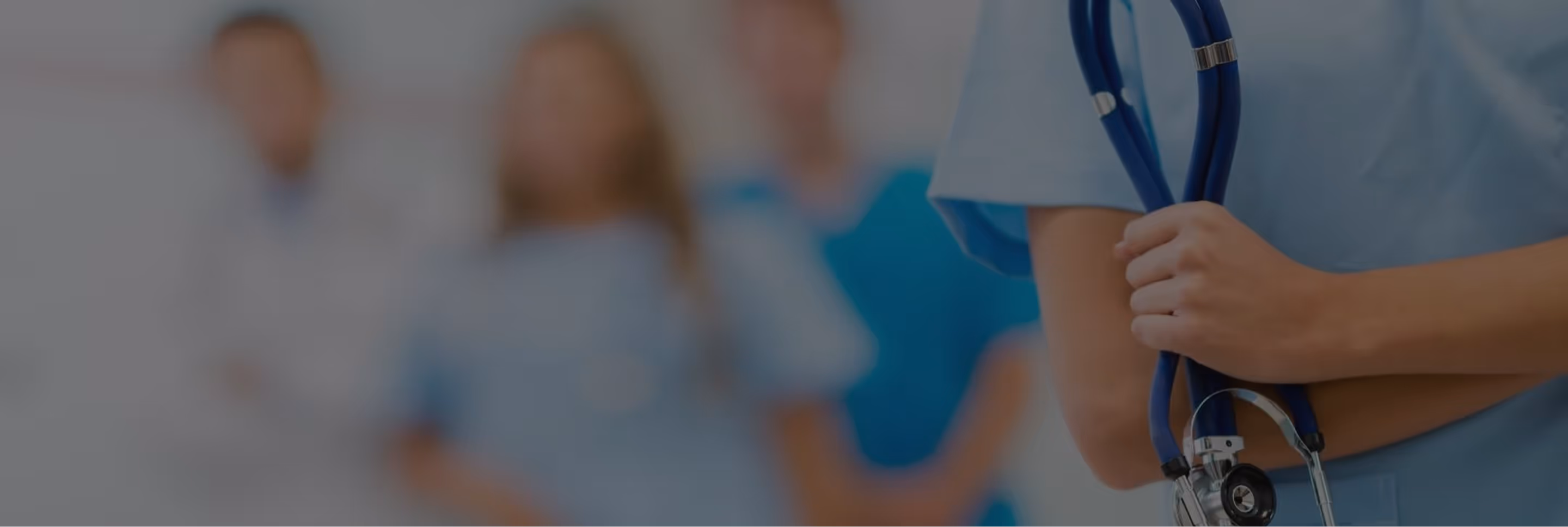 Close-up of a healthcare professional in blue scrubs holding a stethoscope with a blurred group of medical staff in the background.