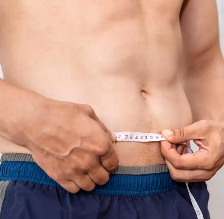 Close-up of a person measuring their waist with a tape measure while wearing blue shorts.