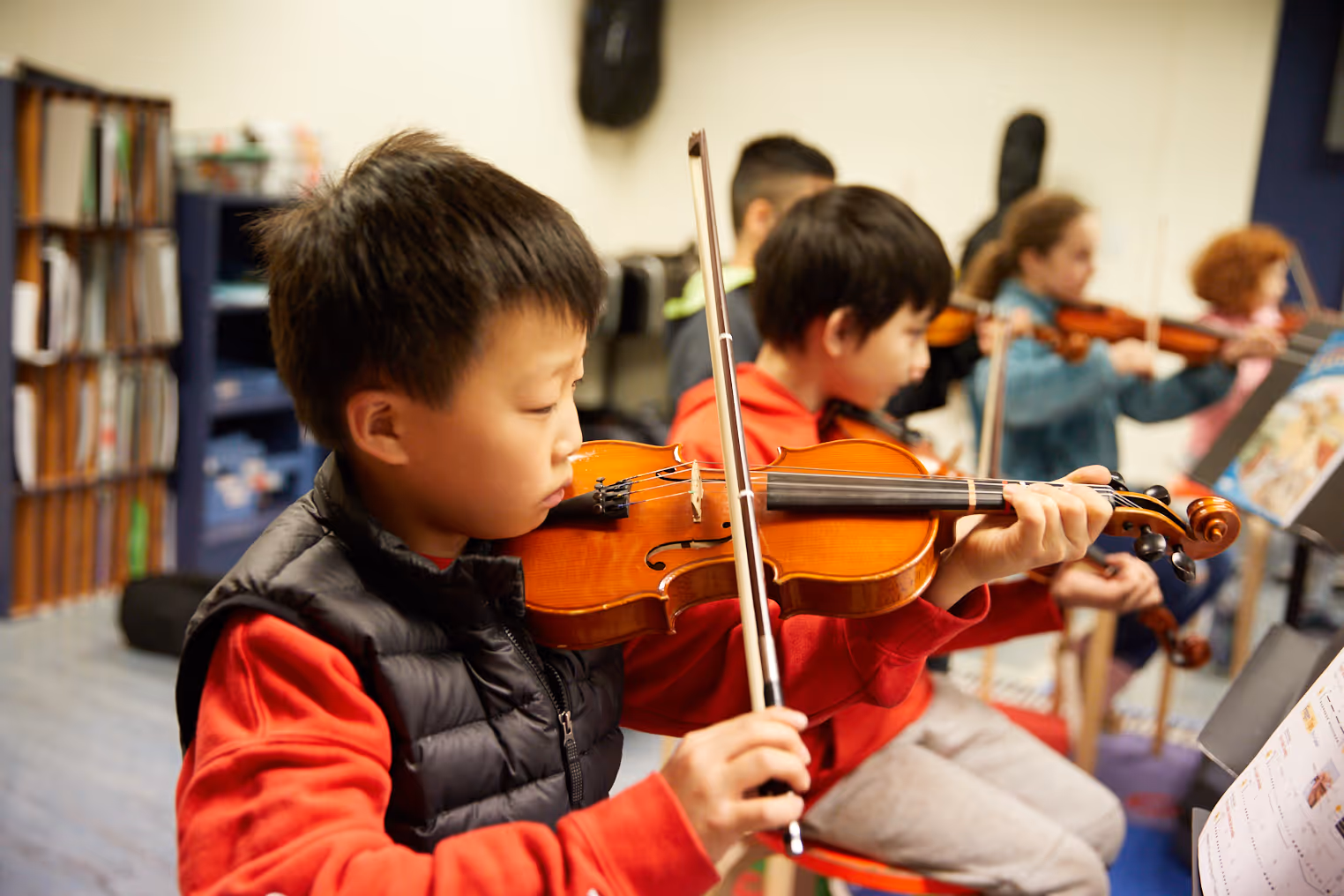 Boy in a black jacket smiling while playing a board game with colorful pegs indoors.