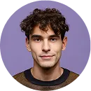 Portrait of a young man with curly dark hair wearing a dark sweater against a purple background.