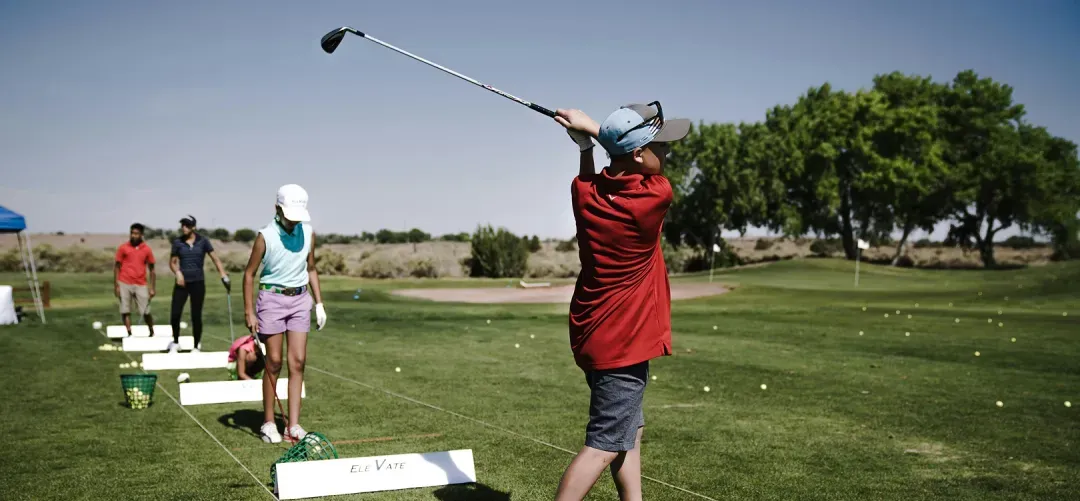 Young people practicing golf swings on a driving range under clear skies.