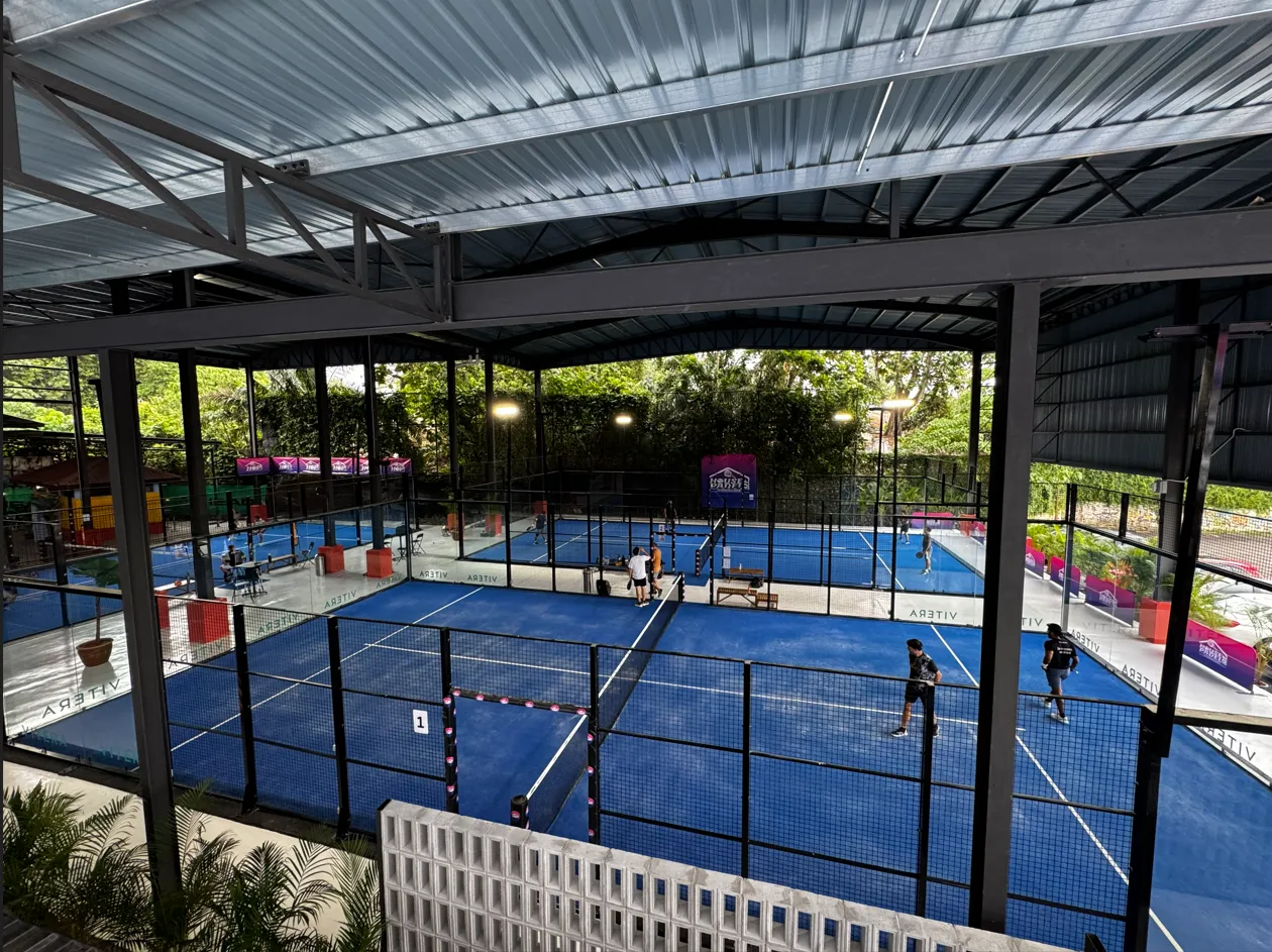 Indoor sports facility with four blue padel courts and players engaged in games.
