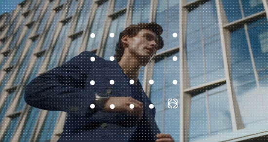 Man in a navy blue blazer standing in front of a modern glass building, looking upwards.