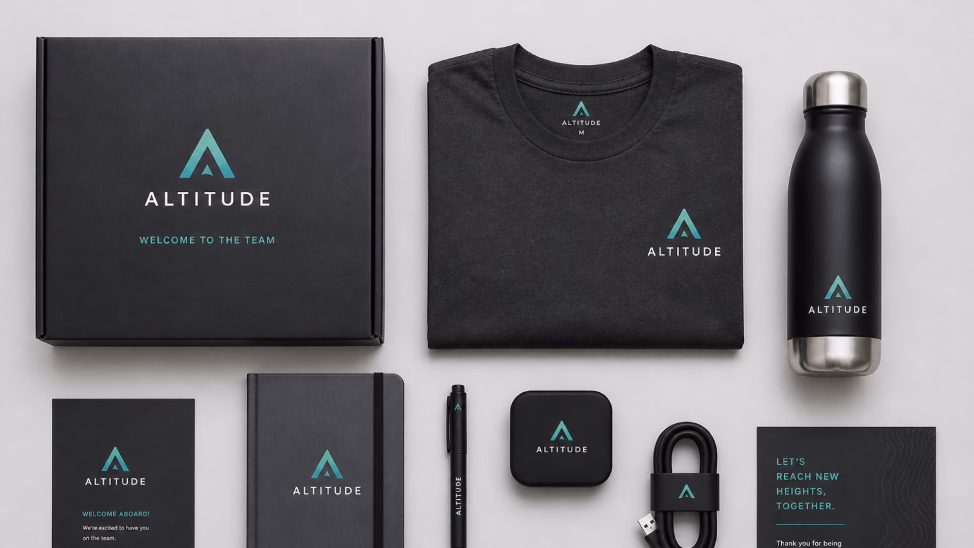 Flat lay of a premium branded employee welcome kit featuring a custom gift box, t-shirt, water bottle, notebook, pen, and tech accessories.