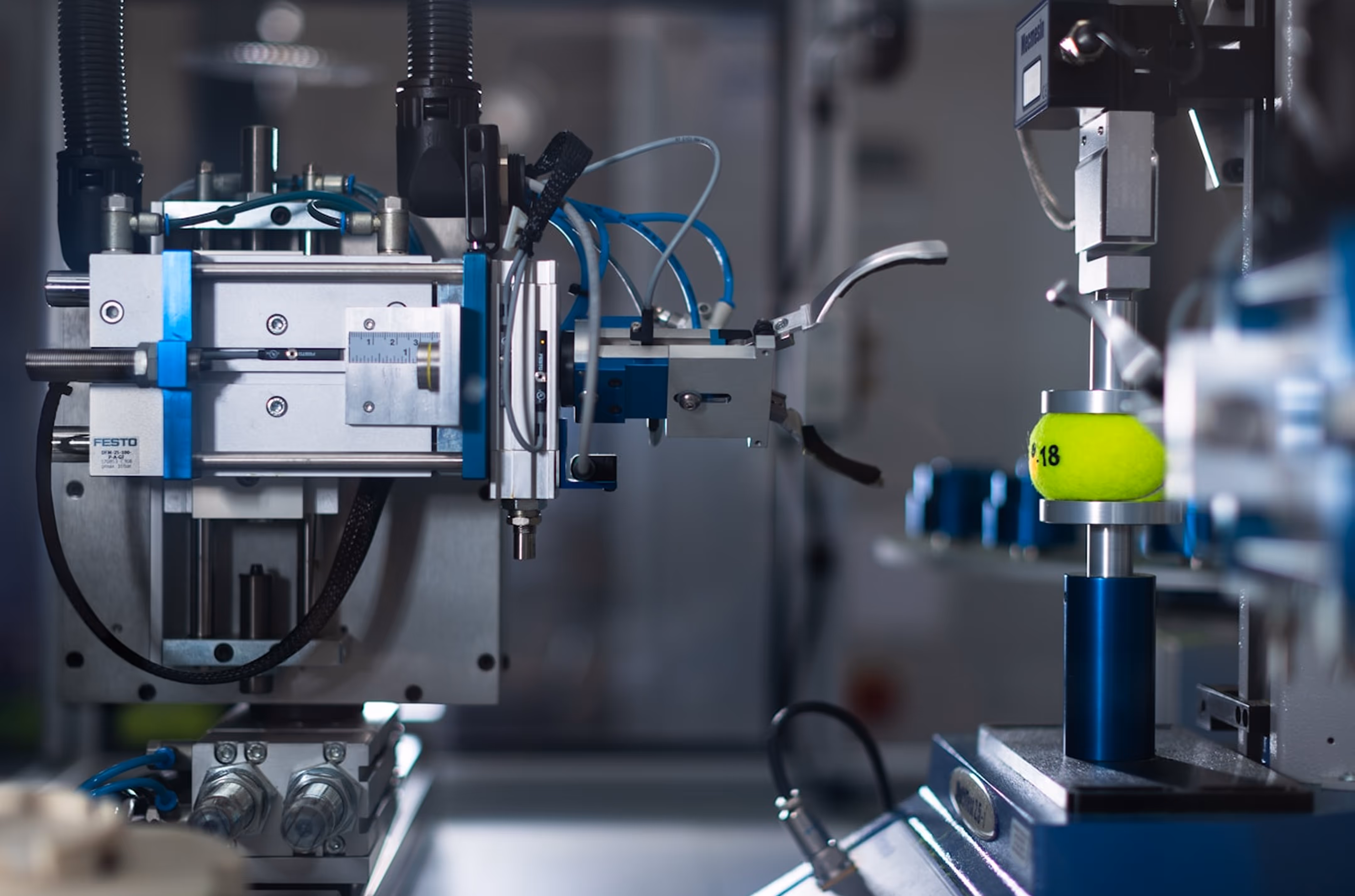 Industrial machine with mechanical arm holding a tennis ball for testing or processing.