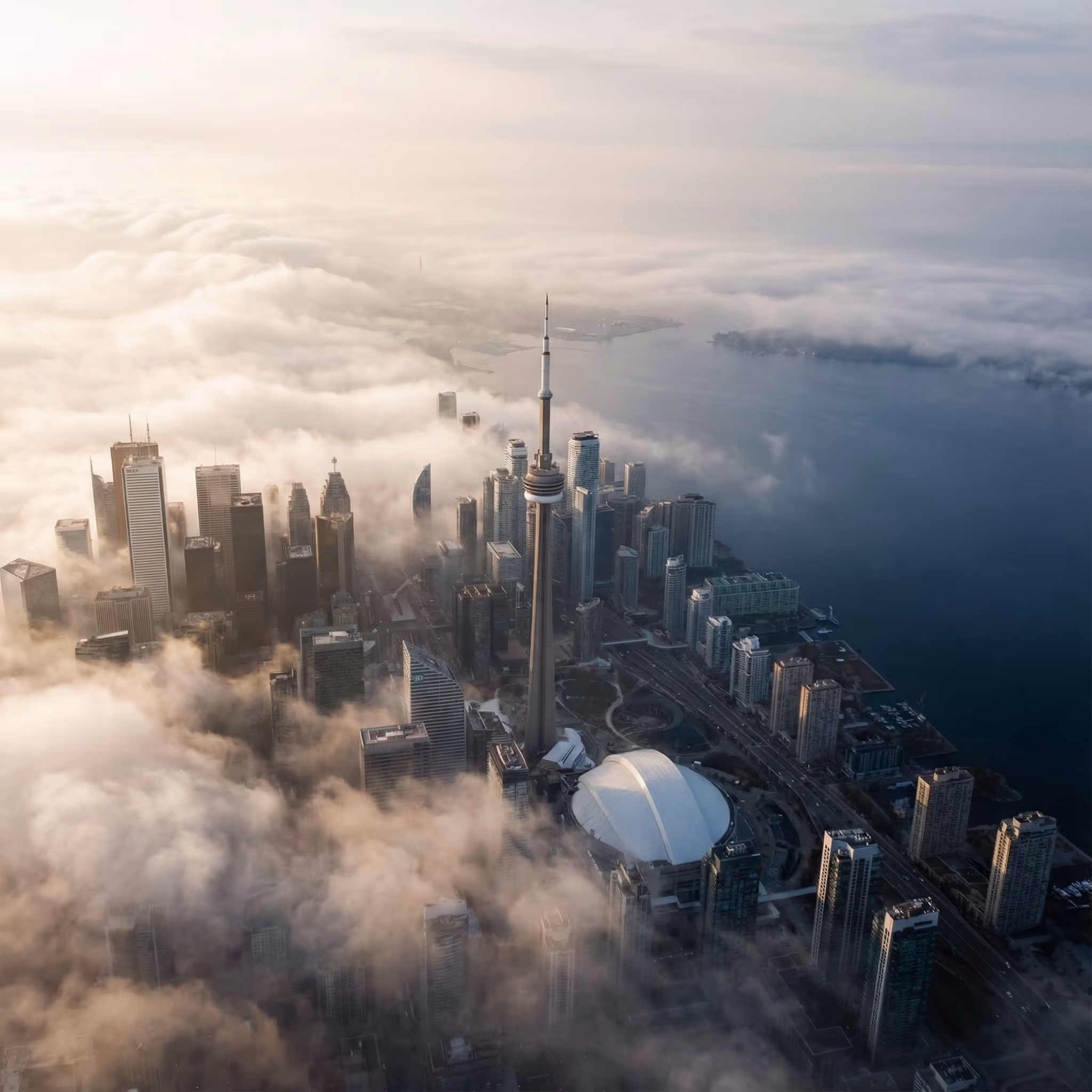 Aerial view of Toronto skyline with CN Tower emerging through morning fog near Lake Ontario.