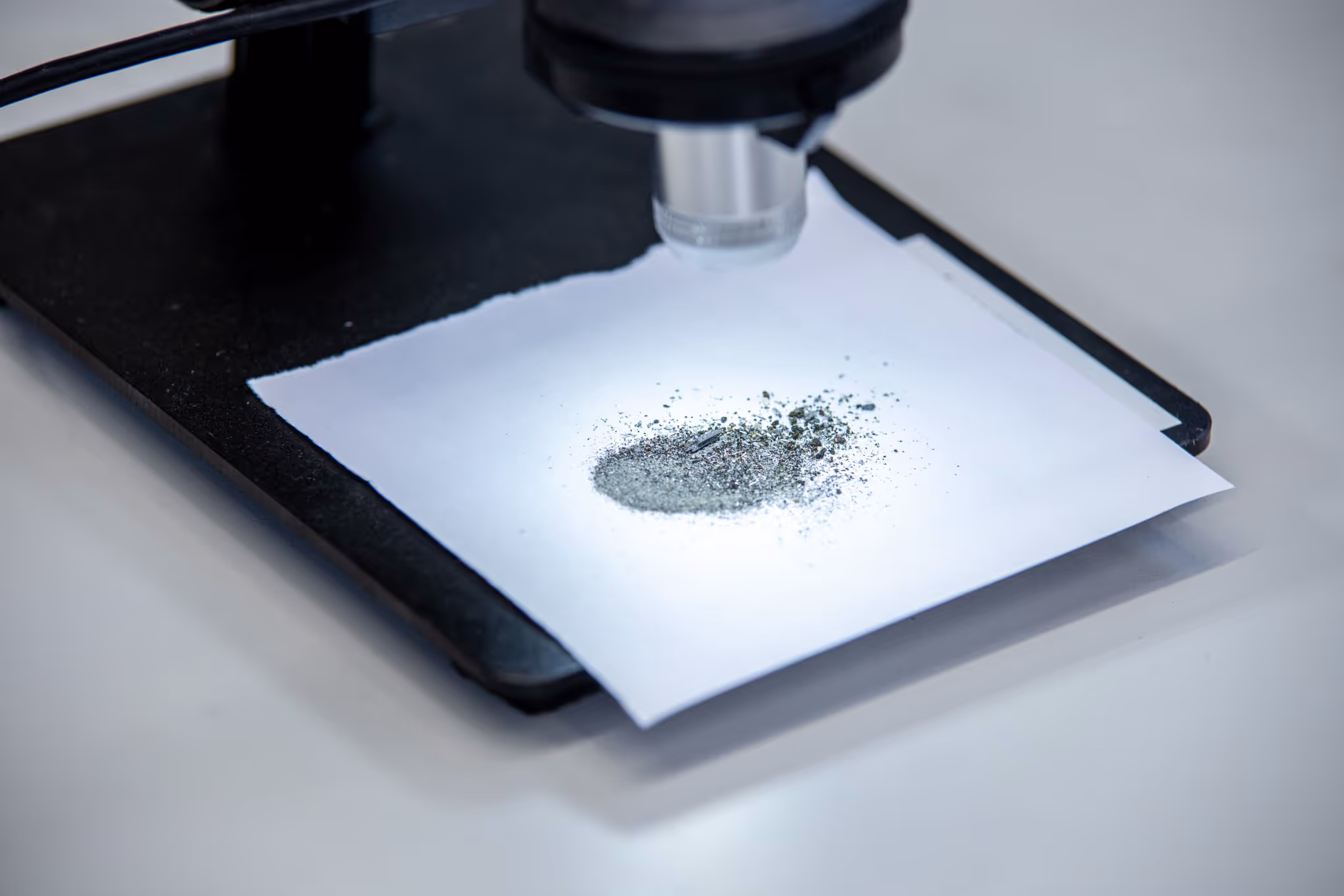 Microscope focusing on a small pile of metallic powder on a white paper.