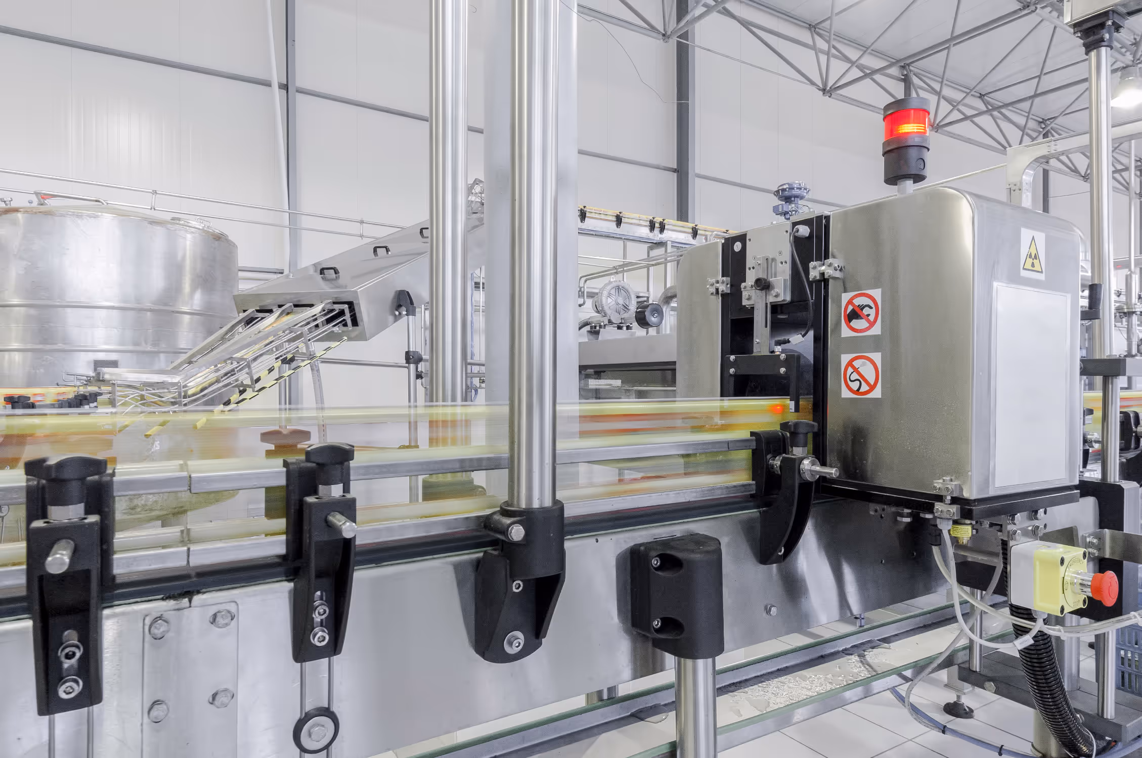 Automated packaging conveyor with motion-blurred bottles passing through stainless steel machinery in a factory setting.
