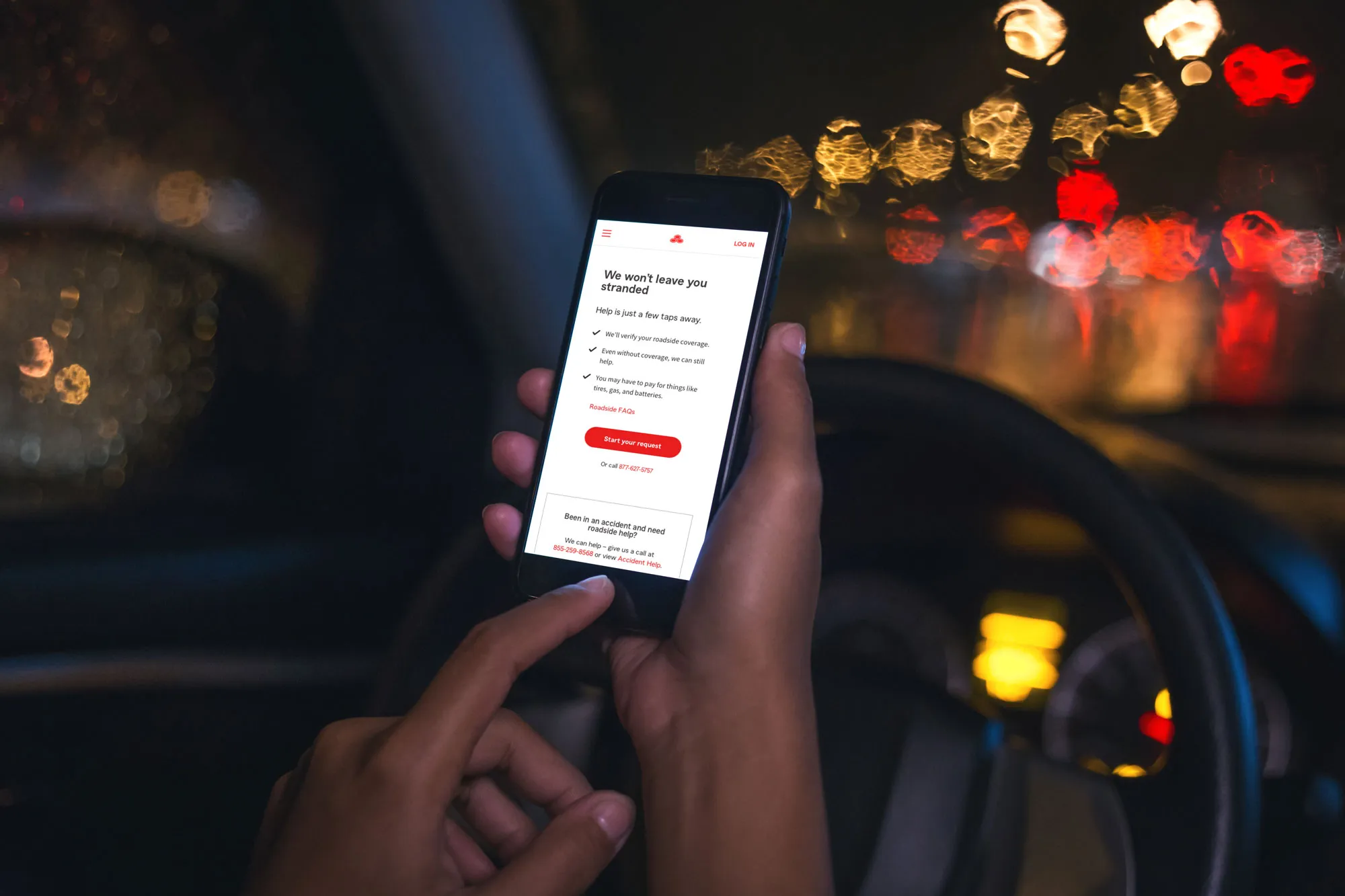 Person using roadside assistance app on a smartphone inside a car at night with blurred traffic lights in the background.