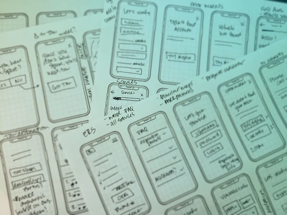 Hand-drawn mobile app wireframe sketches on multiple sheets of paper showing user interface layout and handwritten notes.