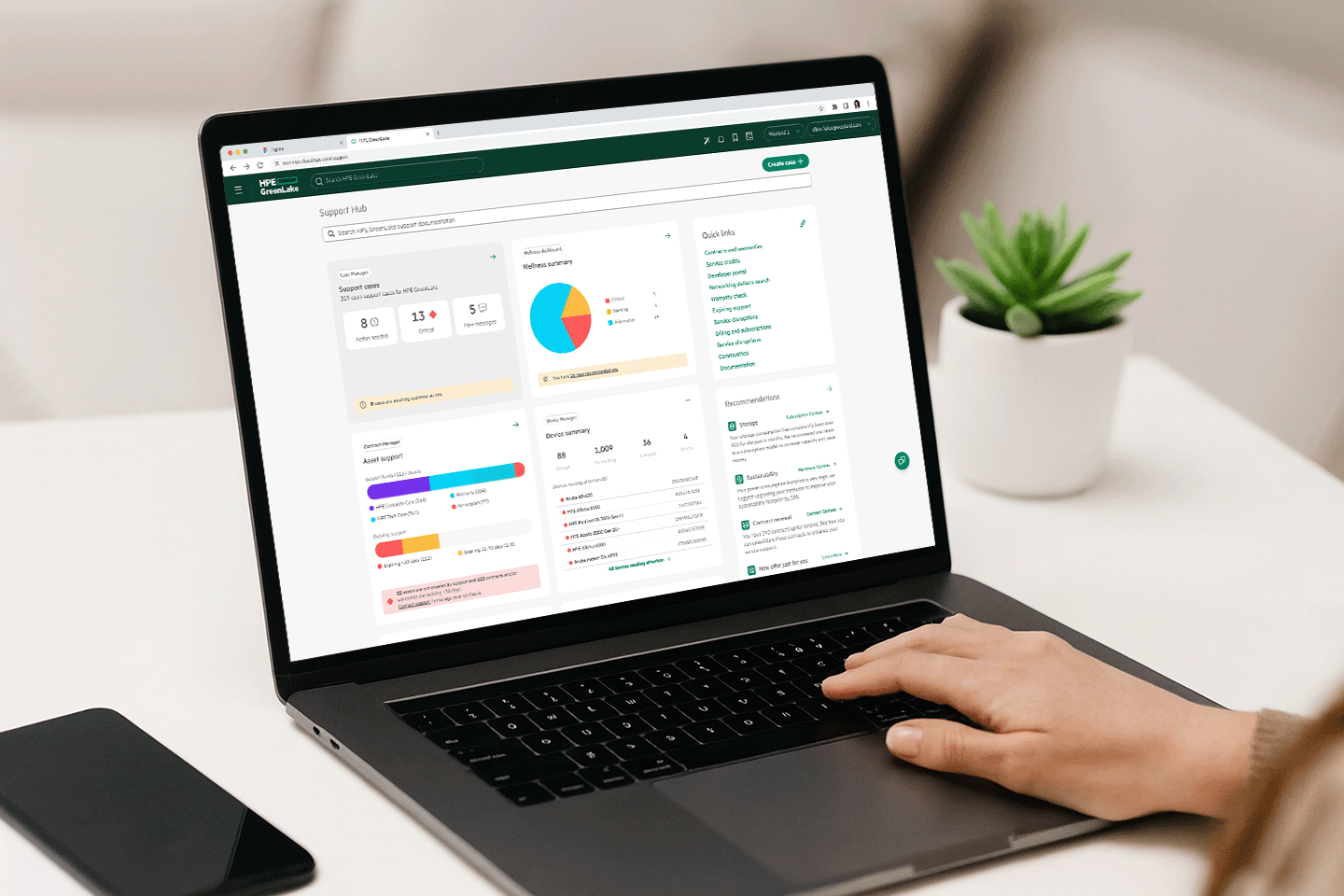 Person using a laptop displaying HPE GreenLake Support Hub dashboard with support cases, wellness summary pie chart, asset support bars, device summary, and quick links.