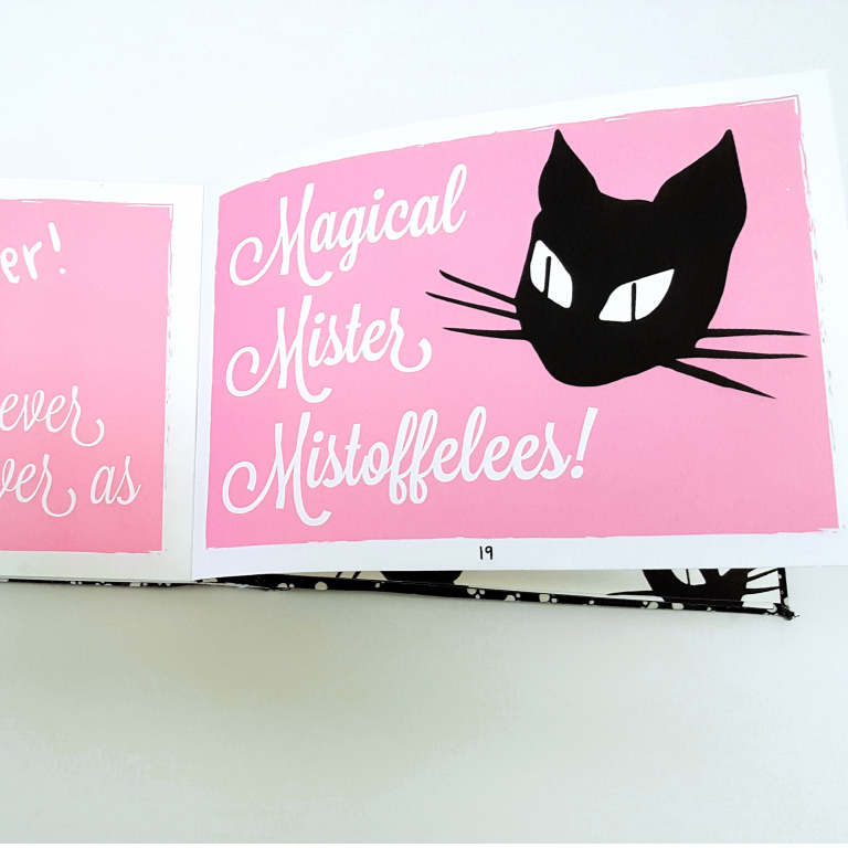 Open book showing a pink page with white cursive text 'Magical Mister Mistoffelees!' and a black cat face illustration.