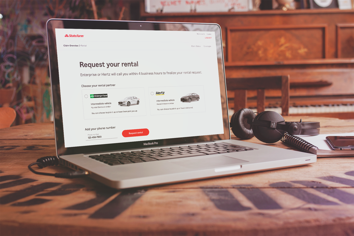 MacBook Pro on wooden table displaying a State Farm webpage to request a rental car from Enterprise or Hertz, with options for intermediate vehicles.