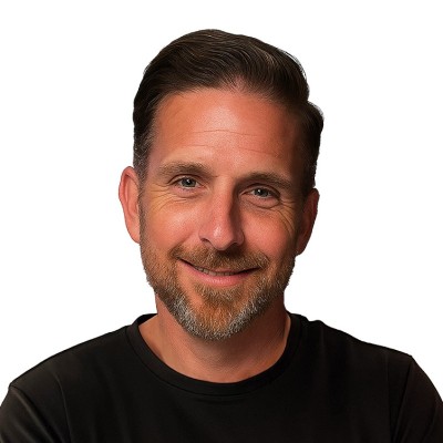 Headshot of a smiling man with short brown hair and a beard wearing a black shirt against a white background.
