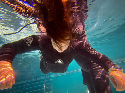 Teilnehmende treibt Kopfüber im Wasser. Hier wird der Tauchreflex trainiert. Partnerin sichert im Hintergrund ab.