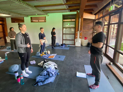 Der Kursleiter Alexander Neubert zeigt den Teilnehmenden die Bauchatmung. Sie stehen auf Yogamatten im Ruheraum des Thermalbades.