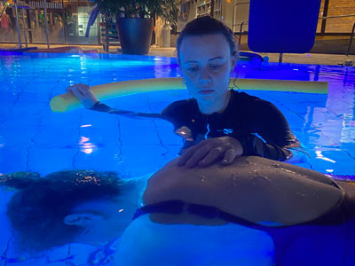 Teilnehmende übt Atempause im Wasser und trainiert Tauchreflex. Partnerin sichert ab und hält körperliche Verbindung aufrecht.