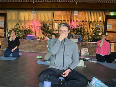 Teilnehmende üben die Wechselatmung Anuloma Viloma. Sie sitzen auf Yogamatten im Ruheraum des Thermalbads.