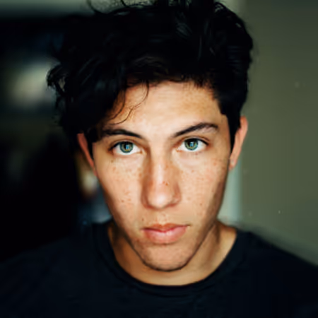 Portrait of a young man with curly dark hair and green eyes looking directly at the camera.
