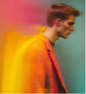Woman in white dress sitting with arms resting on knees in soft lighting.
