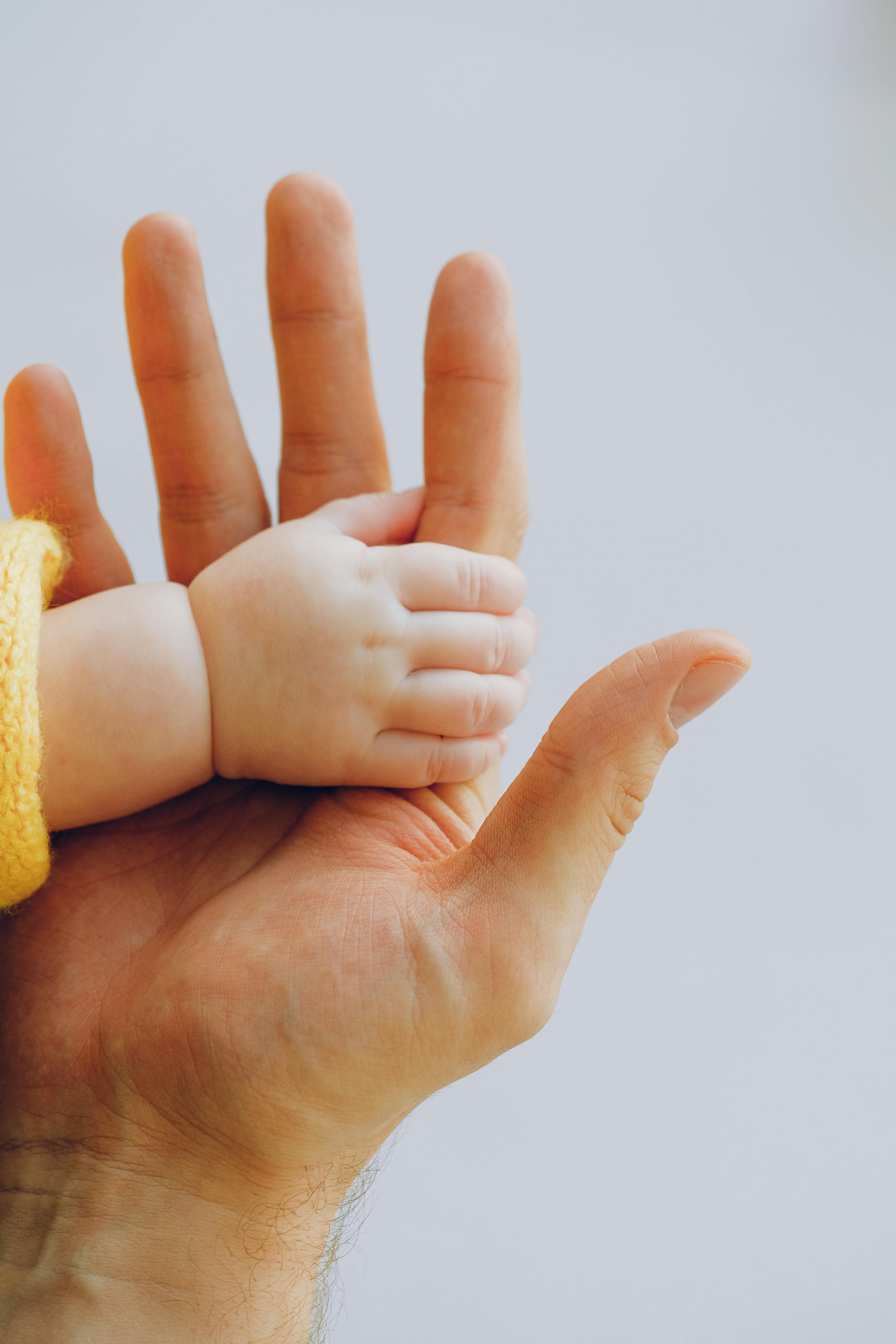 Adult hand holding a baby's hand against a plain light background.