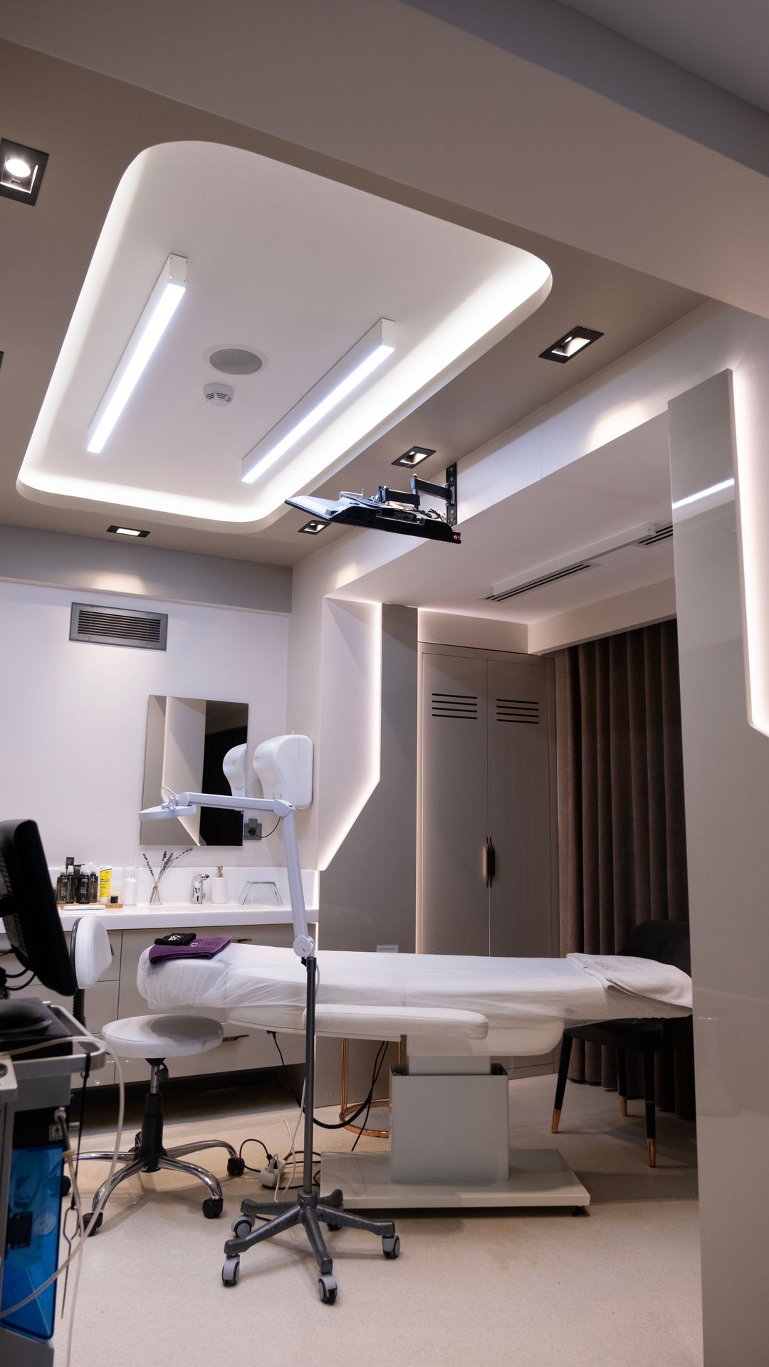 Salle de soins moderne avec fauteuil d'examen blanc, plafond lumineux et équipements médicaux sur roulettes