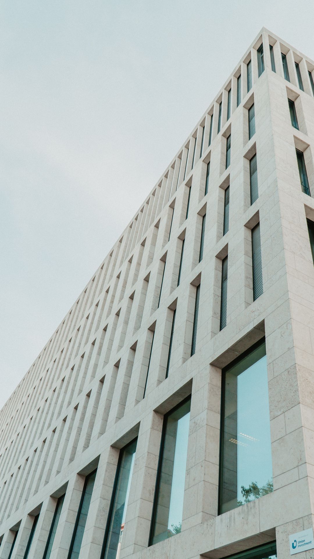 Façade claire d'un immeuble de bureaux moderne aux grandes fenêtres régulières, vue en contre-plongée