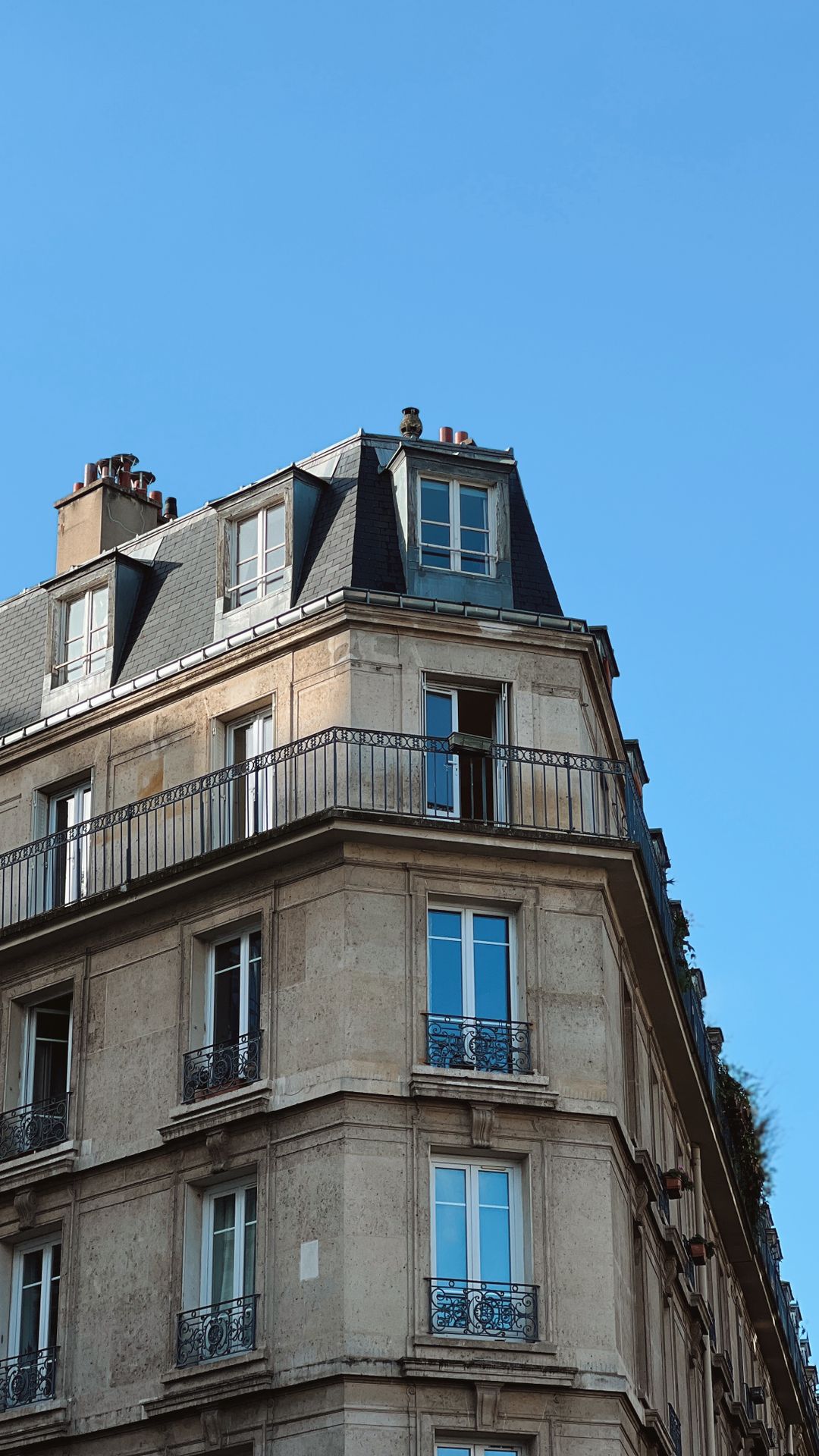 Angle d'un immeuble haussmannien parisien en pierre de taille avec balcons en fer forgé sous un ciel bleu