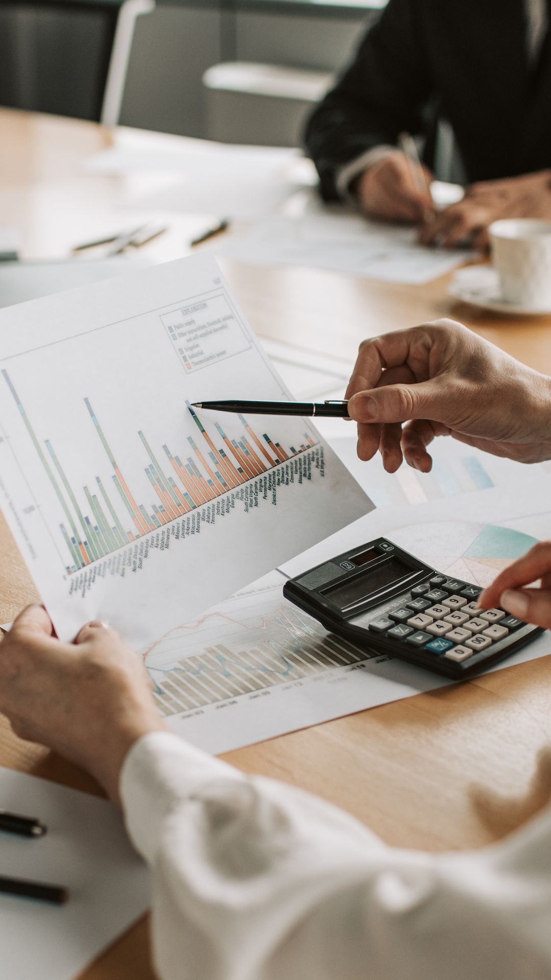 Mains annotant au stylo des graphiques et tableaux de chiffres imprimés, posés sur une table à côté d'une calculatrice