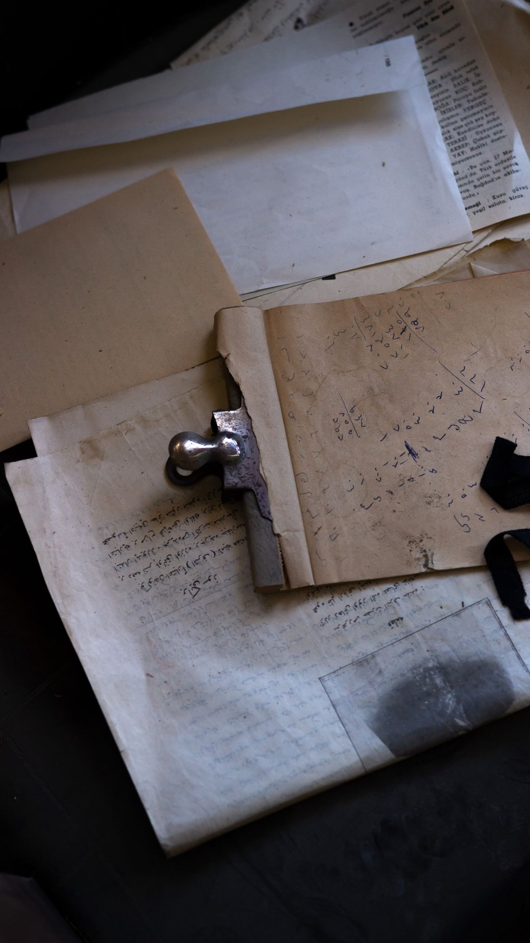Papiers anciens annotés à la main, retenus par une pince métallique et posés sur un fond sombre