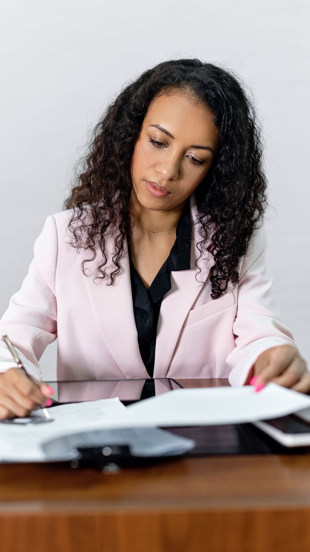 Femme en veste rose relisant et signant un document posé sur un bureau en bois verni