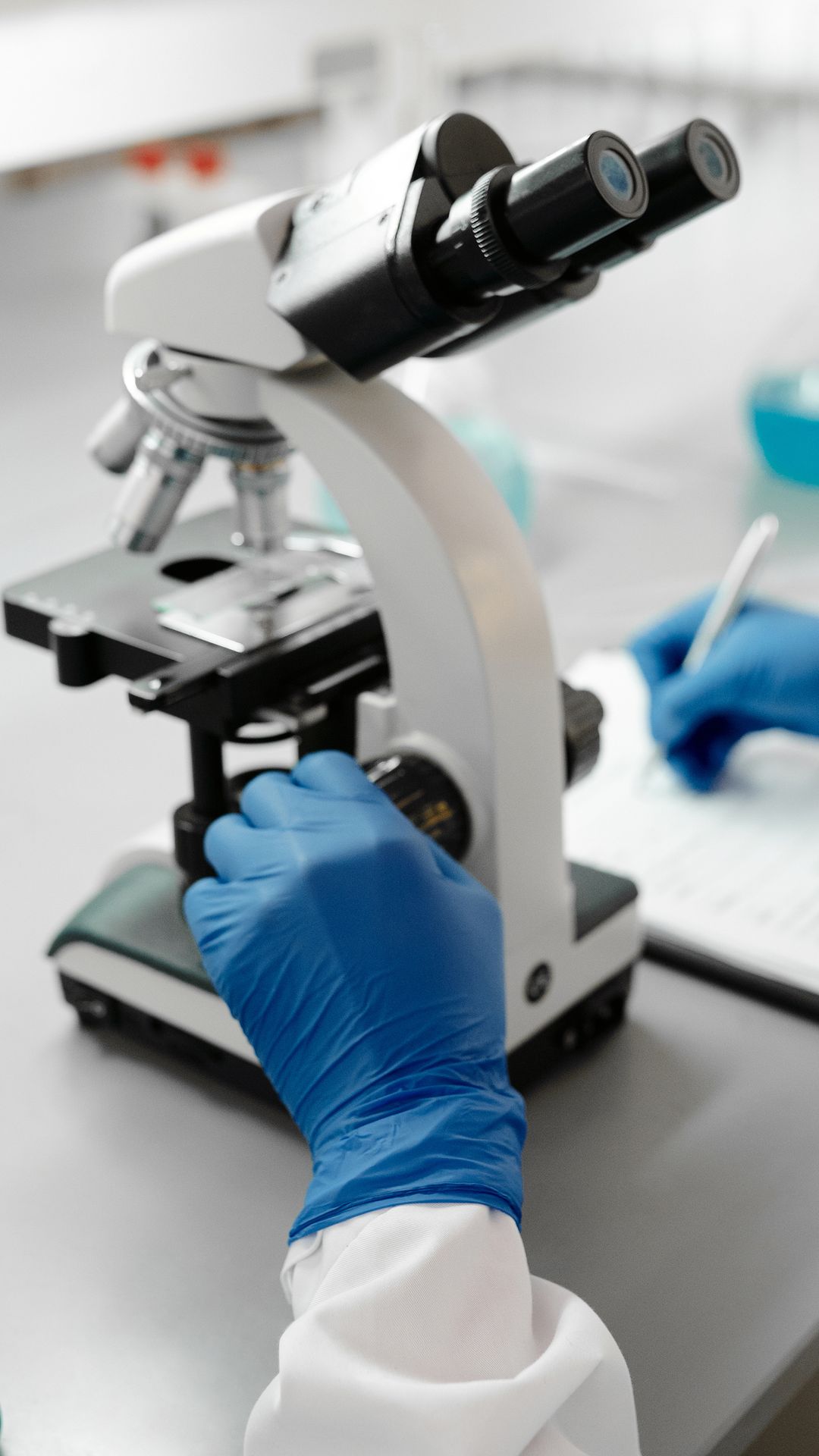 Chercheur en gants bleus réglant un microscope posé sur une paillasse de laboratoire