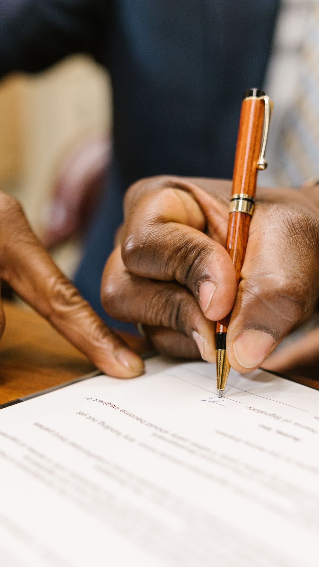 Gros plan d'une main tenant un stylo en bois et signant un document posé sur une table