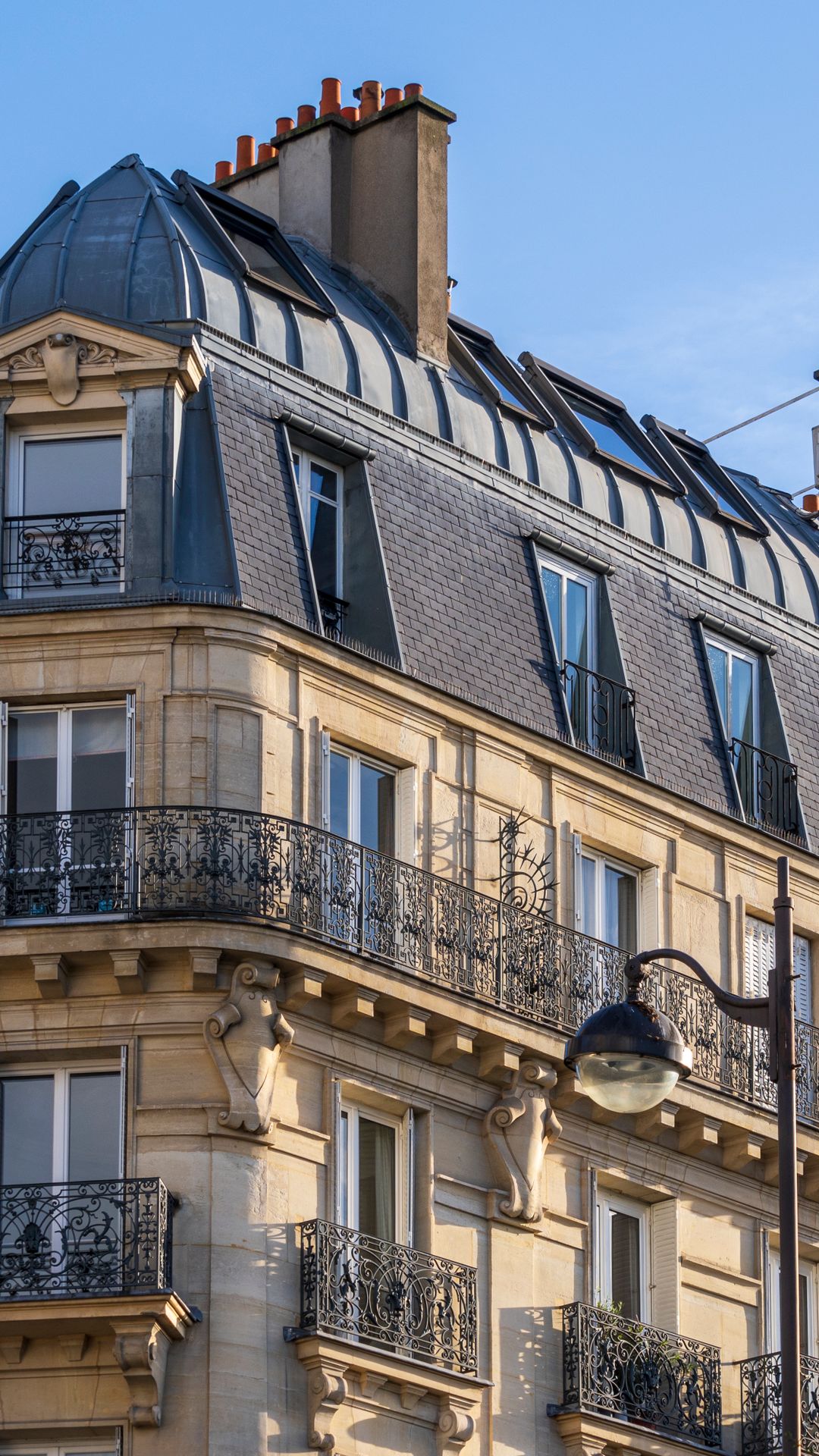 Façade d'un immeuble haussmannien à Paris, balcons en fer forgé et toit d'ardoise sous un ciel bleu