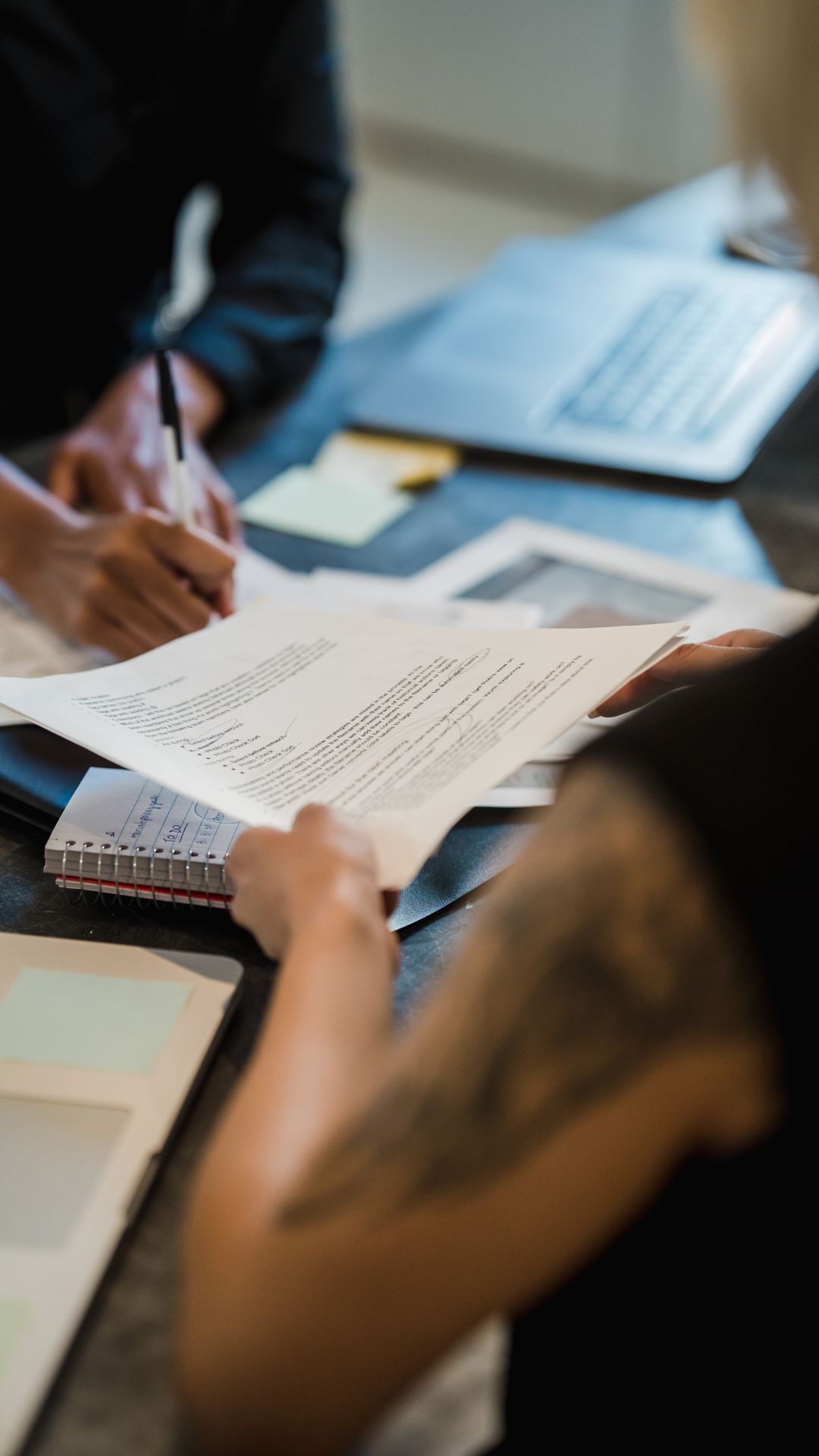 Deux personnes examinent et annotent des documents imprimés sur un bureau, près d'un ordinateur
