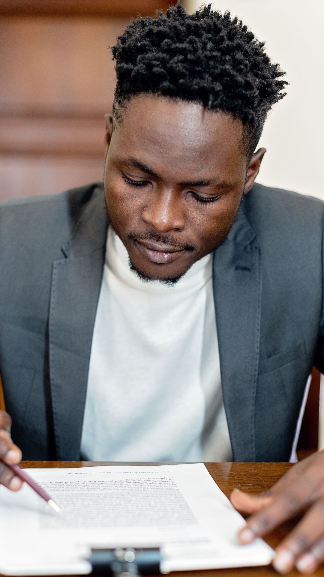 Homme en veste grise et tee-shirt blanc relisant attentivement un document, stylo à la main